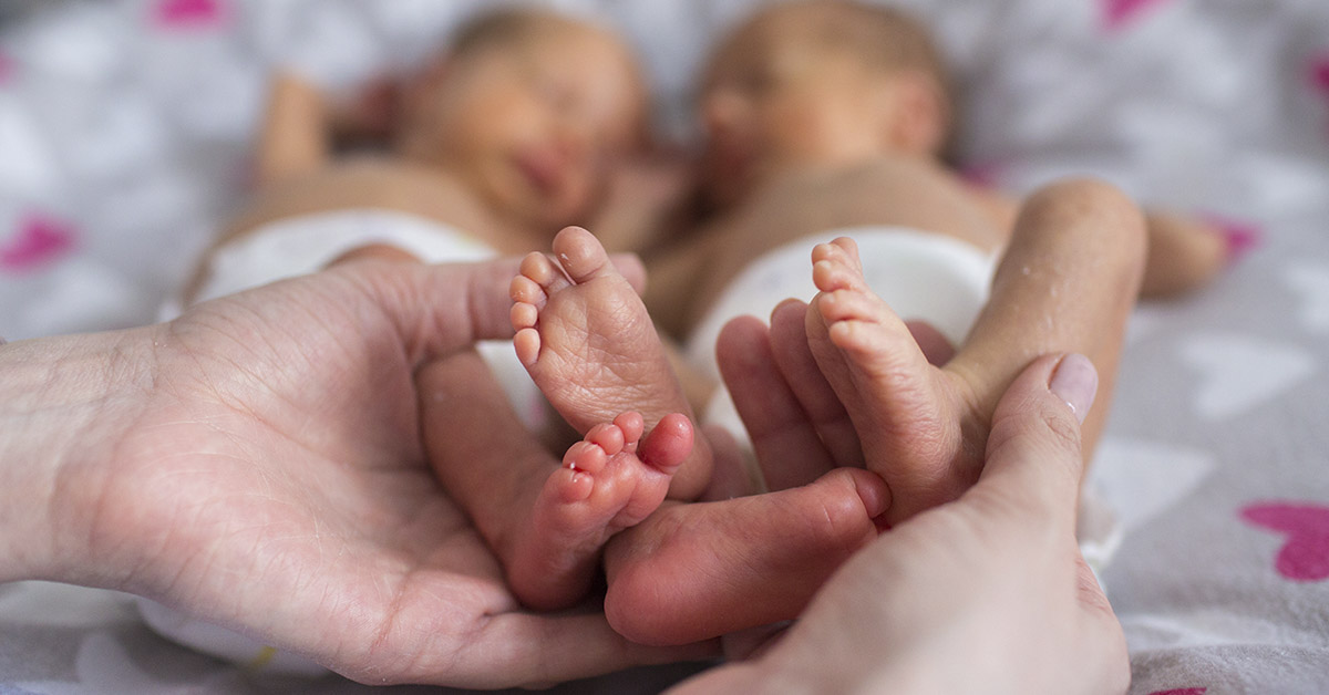 twin infants with feet being held in the hand of an adult
