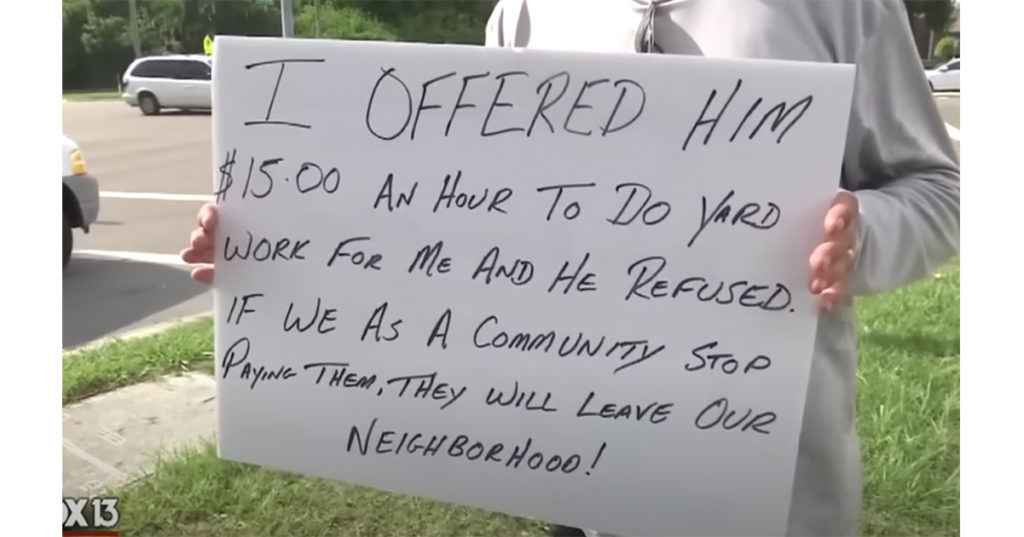 man holding sign offering work to panhandler 