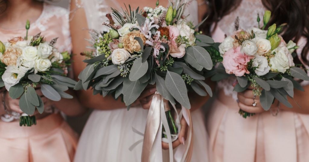 Bridesmaids and bride holding modern wedding bouquets of pink roses and green eucalyptus with pink ribbons. Stylish Contemporary bouquets on soft fabric. Wedding arrangements
