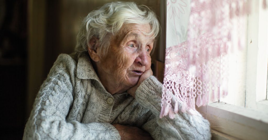 elderly lady sitting at table staring out window