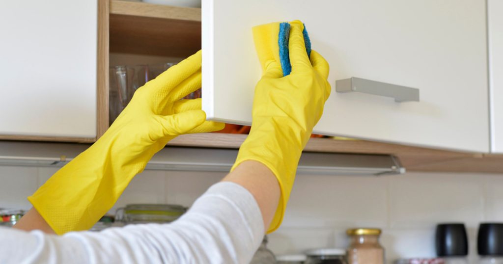 woman in yellow gloves washes the door in kitchen cabinet
