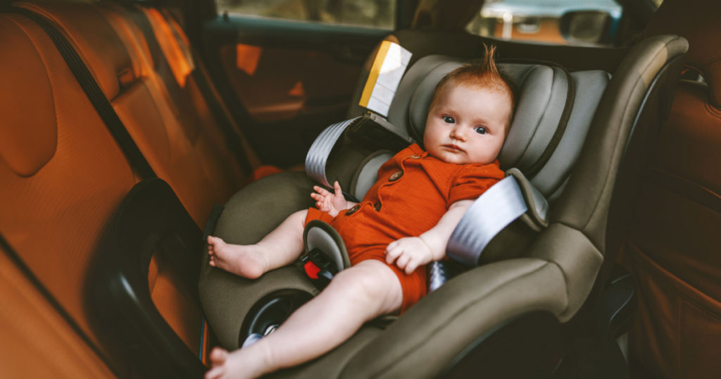 Infant baby sitting in safety car seat child security transportation family lifestyle cute ginger hair kid
