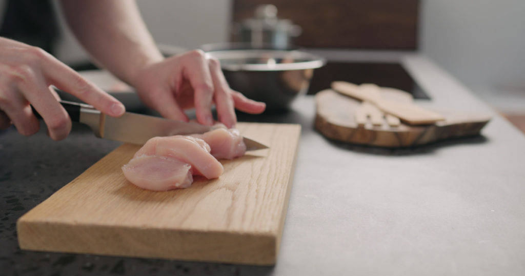 man hands slicing chicken fillet on oak board
