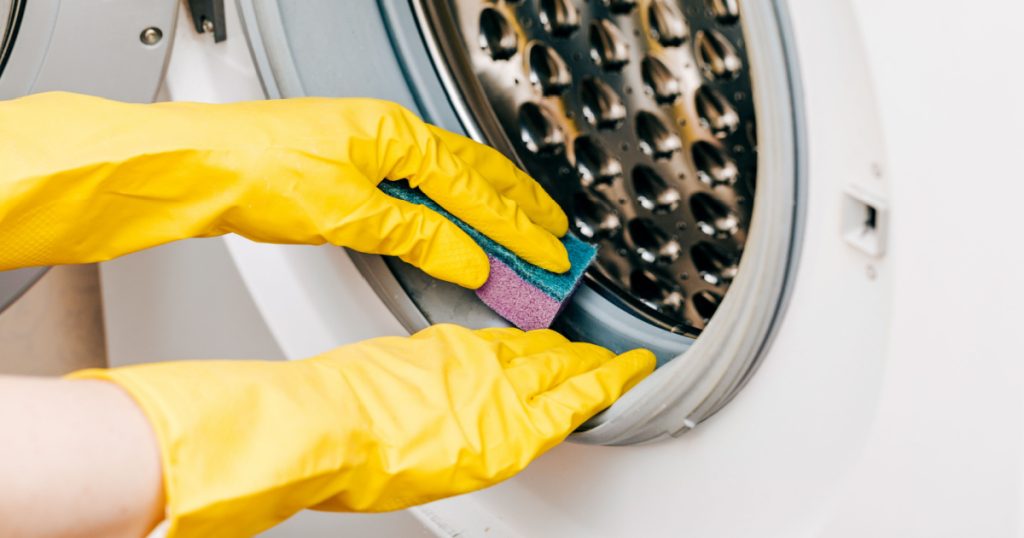 A man in yellow gloves cleans a dirty, moldy rubber seal on a washing machine. Mold, dirt, limescale in the washing machine. Periodic maintenance of household appliances.
