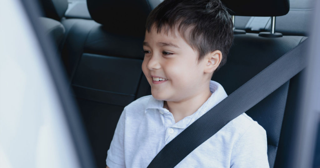 Cinematic portrait boy siting in safety car seat looking out with smiling face,Child sitting in the back passenger seat with a safety belt, School kid traveling to school by car.Back to school

