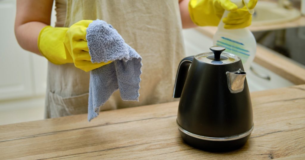 A woman wipes an electric kettle with a rag when cleaning a home kitchen

