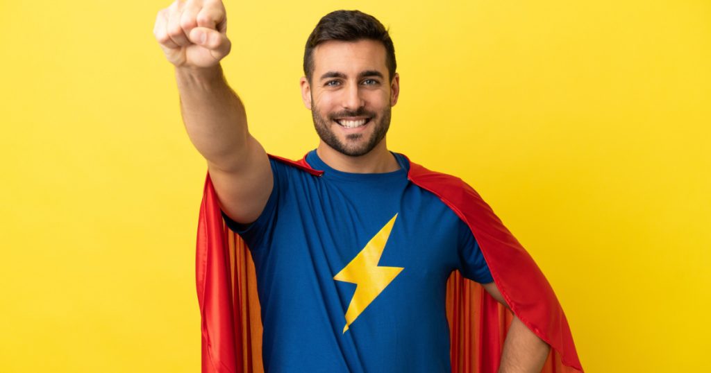 Young handsome caucasian man isolated on yellow background in superhero costume with proud gesture

