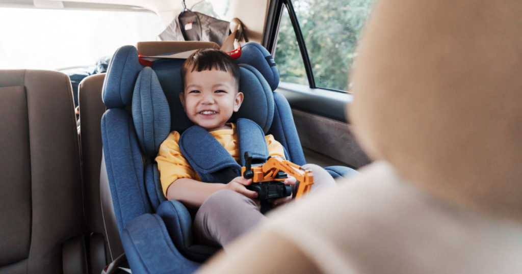 Cheerful smiling Asian little boy in safety car seat, Happy small child travel by car with family.
