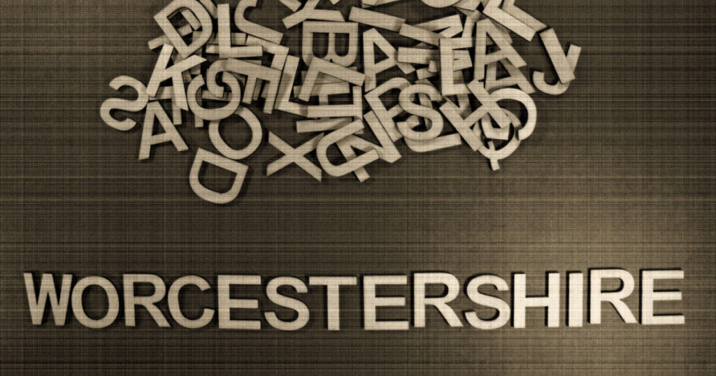 English county name WORCESTERSHIRE in wooden English language capital letters spilling from a pile of letters on a green background in sepia
