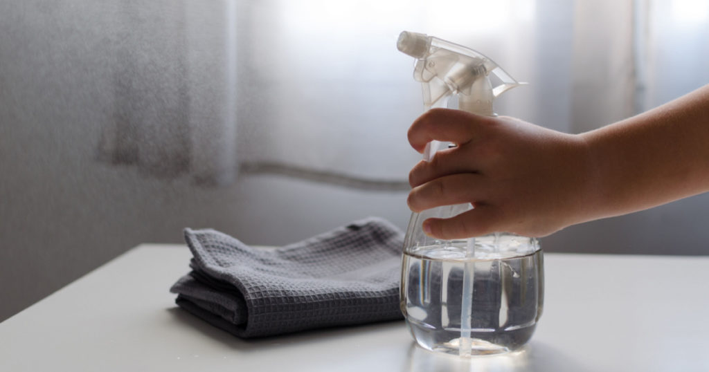 Child's hand squeezing eco cleaning bottle spray filled with water and vinegar. Concept of environmentally friendly home and zero waste, recycling and natural lifestyle
