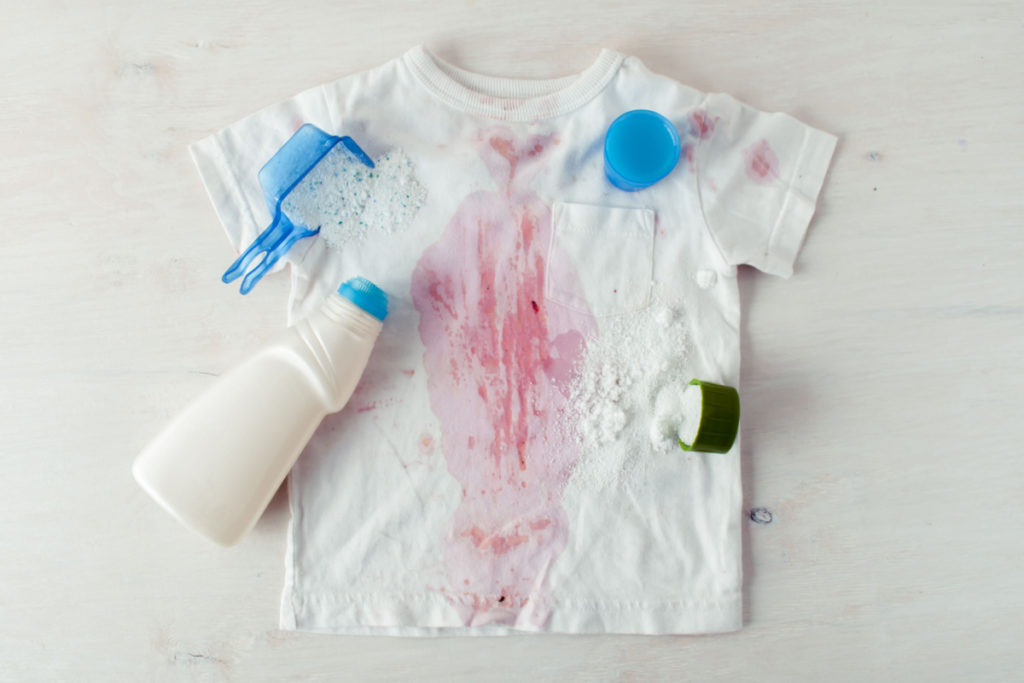 dirty child clothing with red sause spots and variety of detergents on top