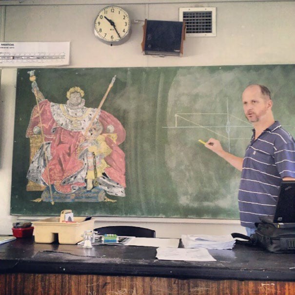 Teacher with blackboard art by his side.