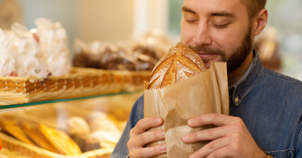 Close up of a young bearded man smelling delicious freshly baked bread at the bakery store copyspace enjoyment pleasure aromatic freshness oven customer buying consumerism retail baking.
