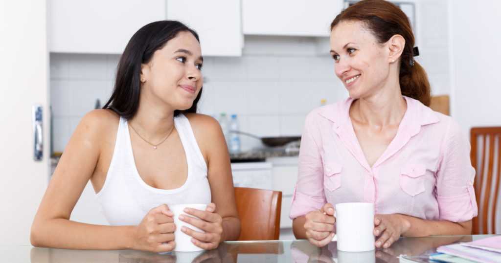 Mother and her teenage daughter talking at kitchen table
