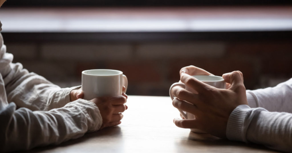 Close up woman and man sitting in cafe, holding warm cups of coffee on table, young couple spending weekend in cozy coffeehouse together, romantic date concept, visitors drinking hot beverages

