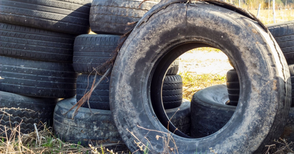 A pile of worn car tires dumped on the field. Environmental pollution. Landfill of used tires, car waste. Car waste recycling, automotive industry. Used tires close up, lie on top of each other
