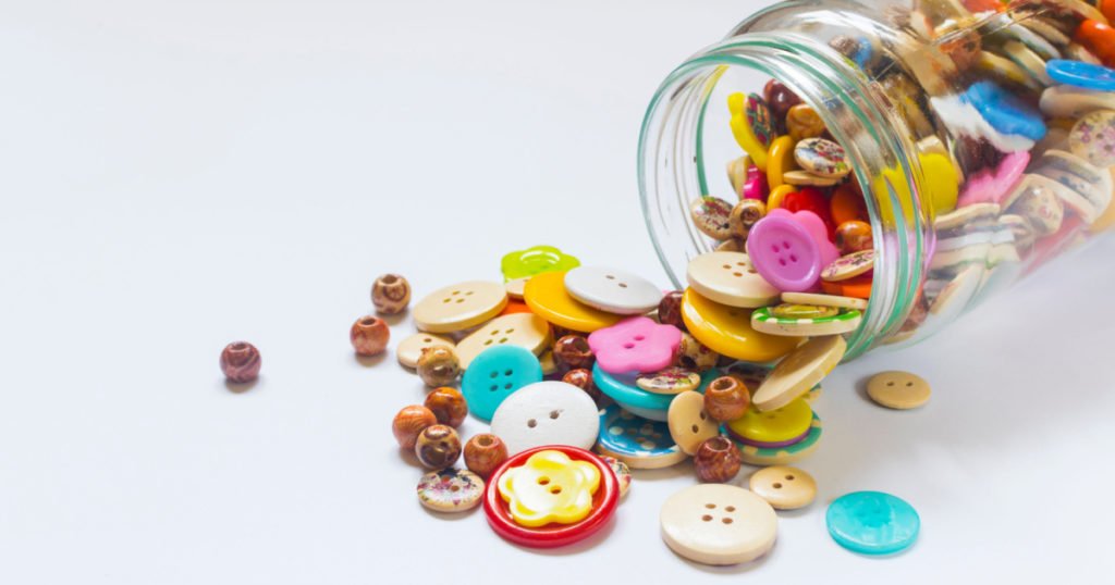 Spilled Jar of Colorful Buttons against a White Background
