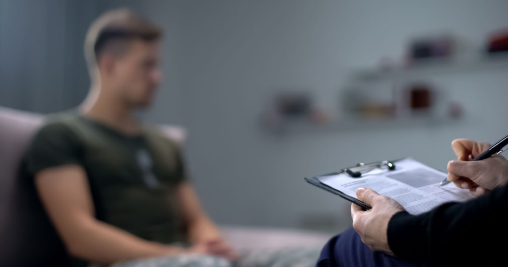 Psychologist making notes during therapy session with sad male soldier, PTSD

