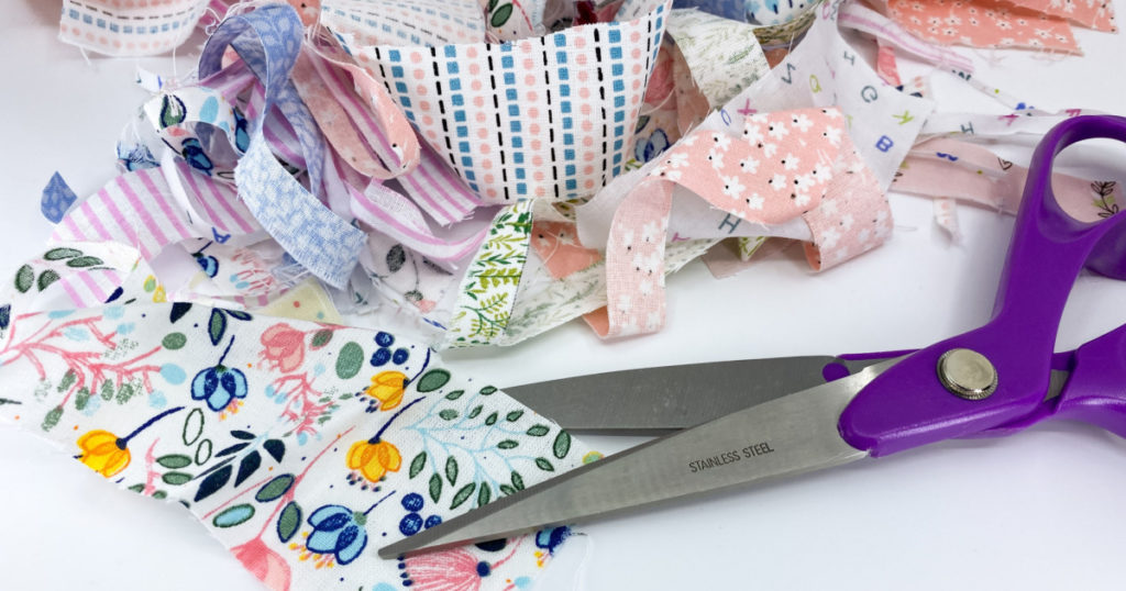 Close up view of a dressmaking scissors with a pile of scraps of printed patterned fabric
