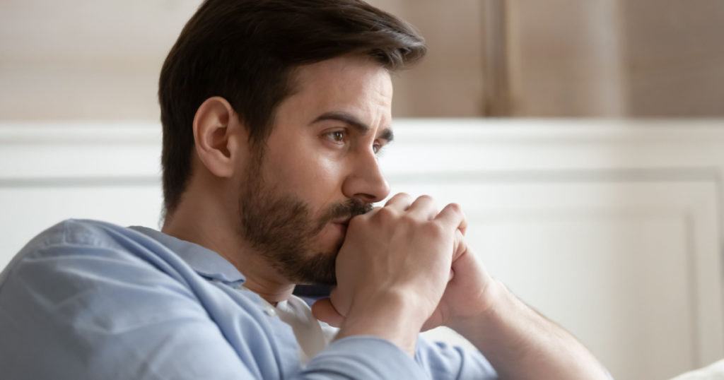 Close up head shot young thoughtful man looking away. Pensive millennial bearded guy thinking of problems, feeling stressed, sitting alone on couch at home, worrying about personal troubles.
