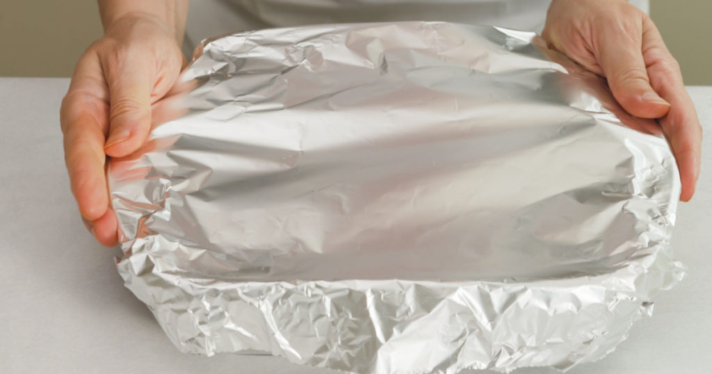 Chef wraps baking pan with aluminum foil. Baking process
