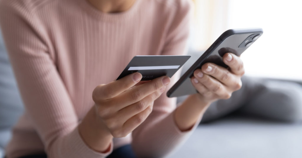 Close up female hands holding credit card and smartphone, young woman paying online, using banking service, entering information, shopping, ordering in internet store, doing secure payment
