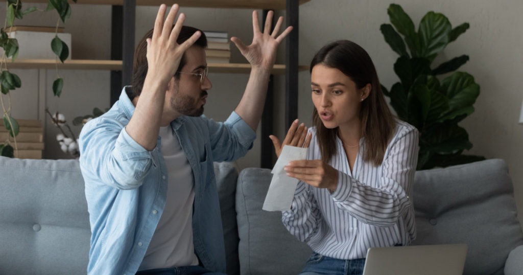 Stressed emotional couple arguing fighting when checking financial papers together finding unexpected debt lack of money on bank account. Mad angry husband scolding wife for overspending family budget
