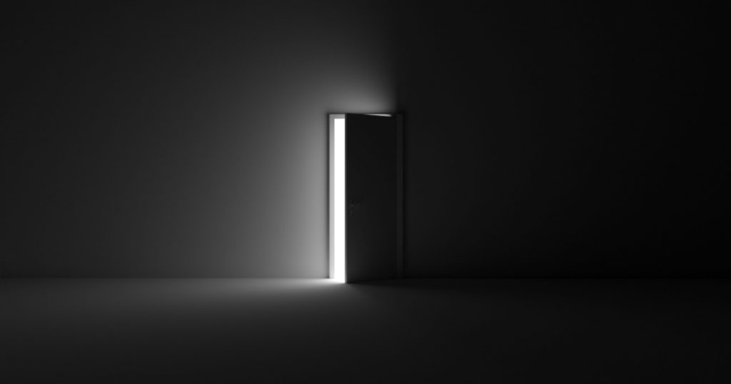 A grayscale shot of an open door letting light into a dark room
