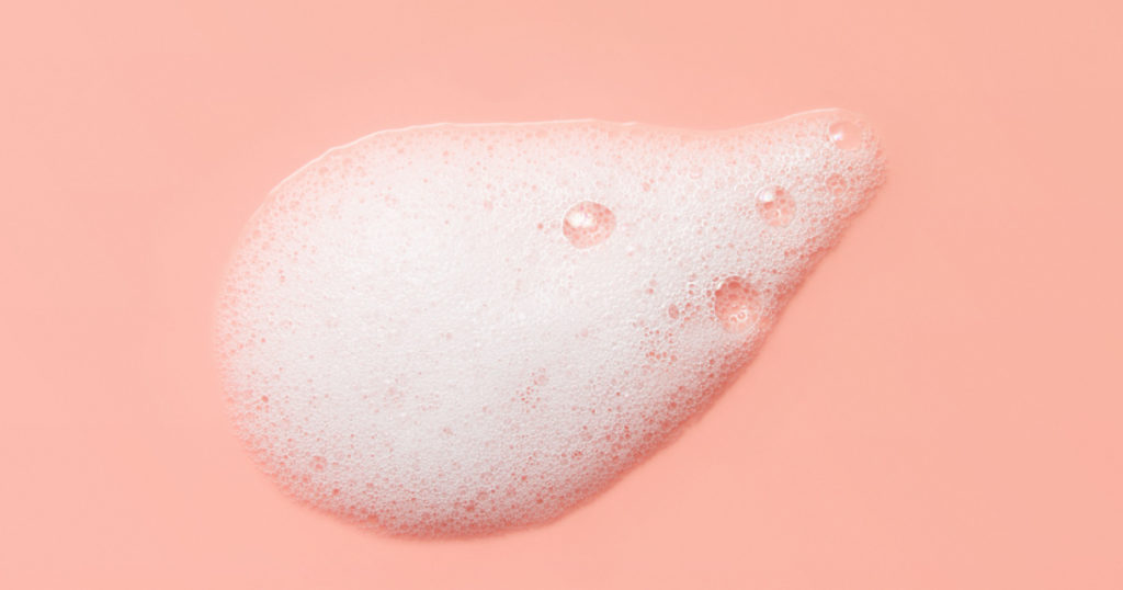 Skincare cleanser foam texture. Soap, shampoo, cleansing mousse bubbles swatch on pink color background. Face wash lather closeup
