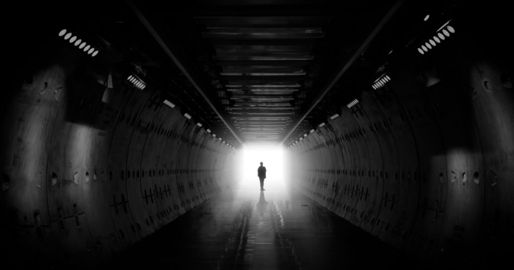 Dreaming, man in dark tunnel. Freedom light in tunnel. Silhouetted desaturated. Silhouette of a woman walking into the light. Light at the end of the tunnel. business man in silhouette walking
