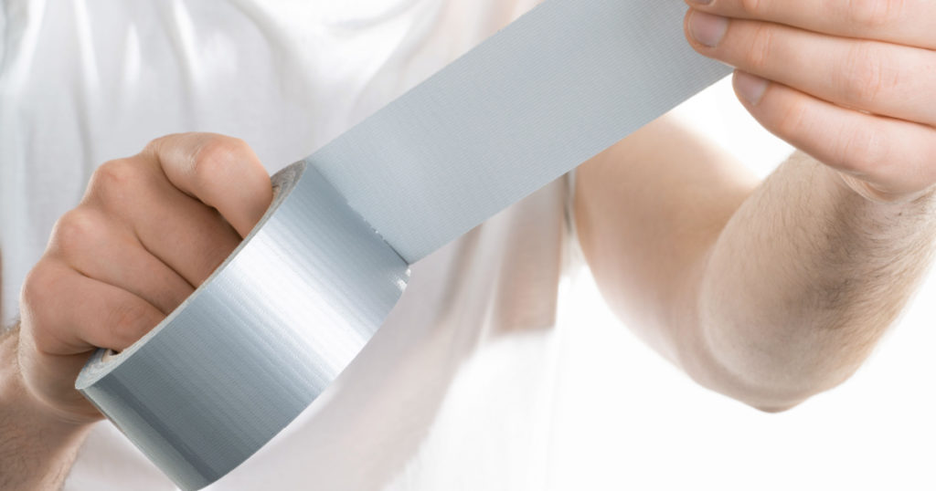 Close up image of man holding adhesive duct tape white background. male hands trying to fix something.
