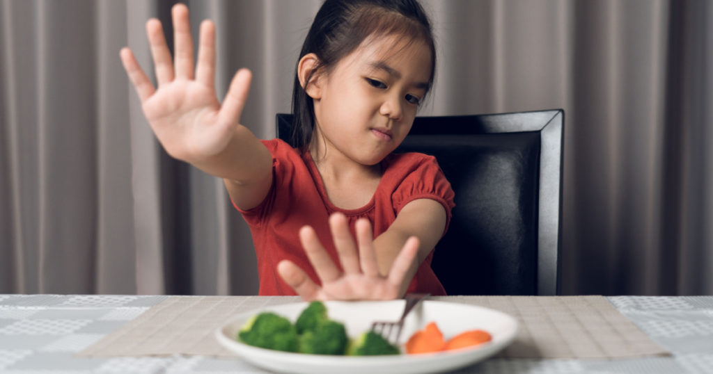 Little cute kid girl refusing to eat healthy vegetables. Children do not like to eat vegetables.
