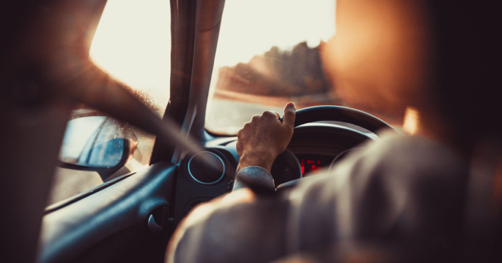 Man driving car, hand on steering wheel, looking at the road ahead,sunset.
