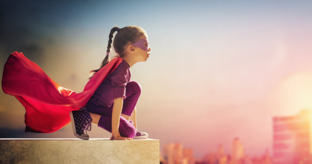 Little child girl plays superhero. Child on the background of sunset sky. Girl power concept
