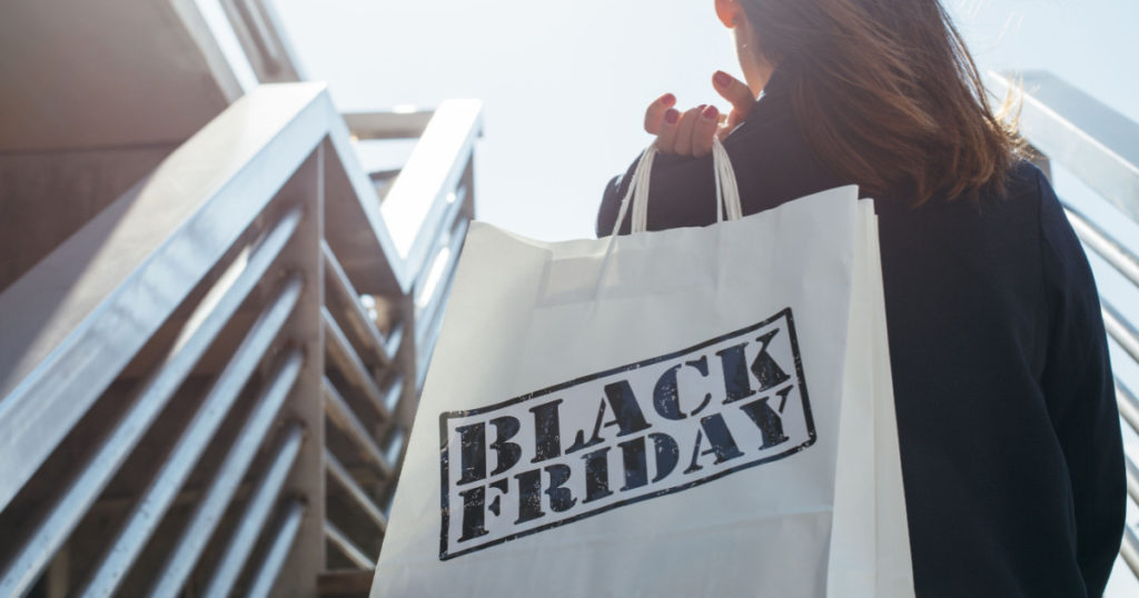 Rear view of incognito brunette holding Black Friday shopping bag while standing outdoors. Copy space