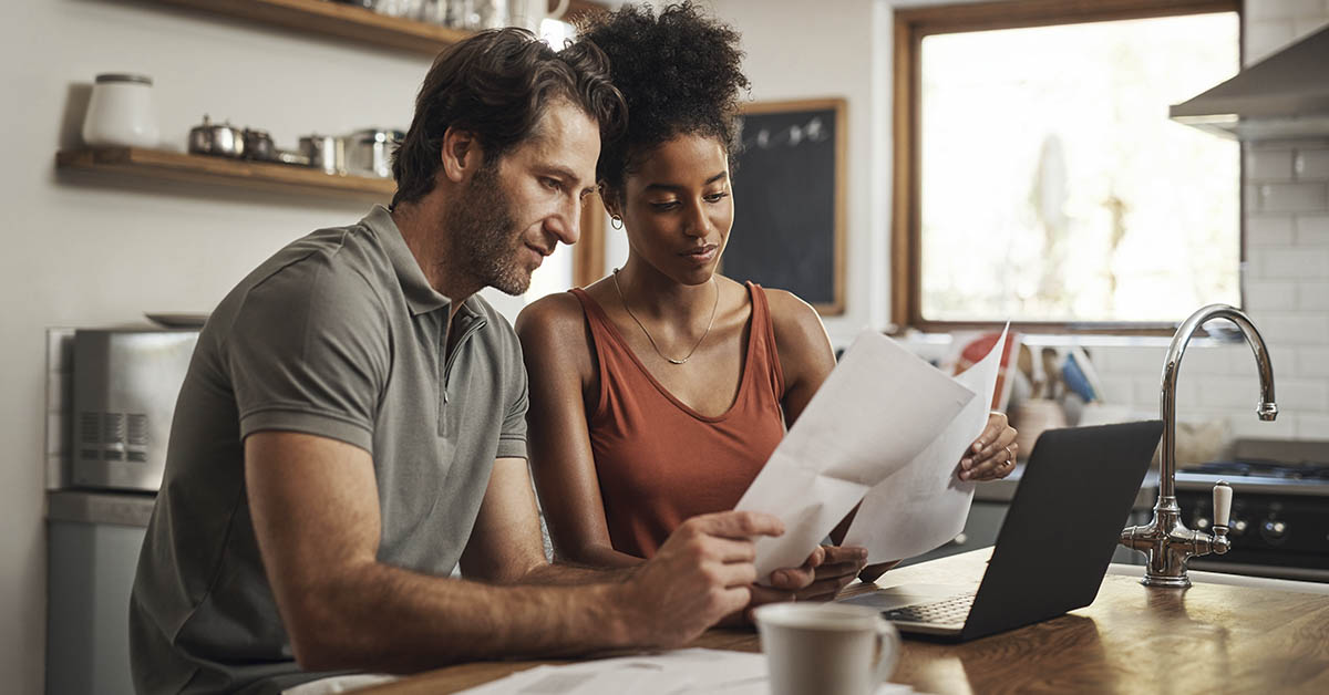 couple sitting at kitchen table looking at papers. Financial health concept