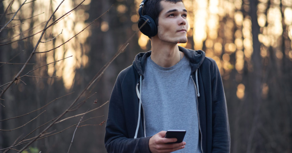 A young millennial man walks in an autumn park and listens to music with headphones. Autumn portrait . Black hoodie, Caucasian model
