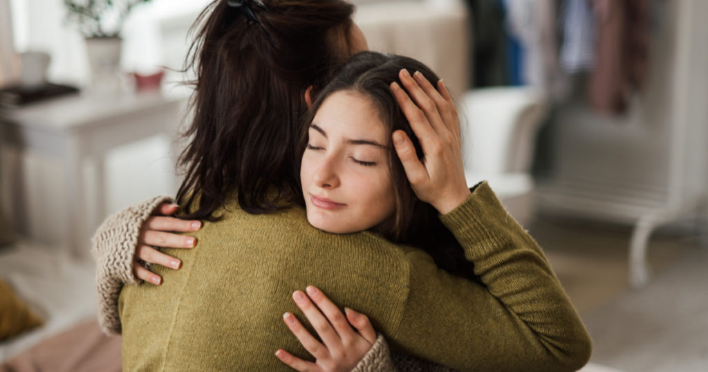Teenage girl hugging her mother at home.
