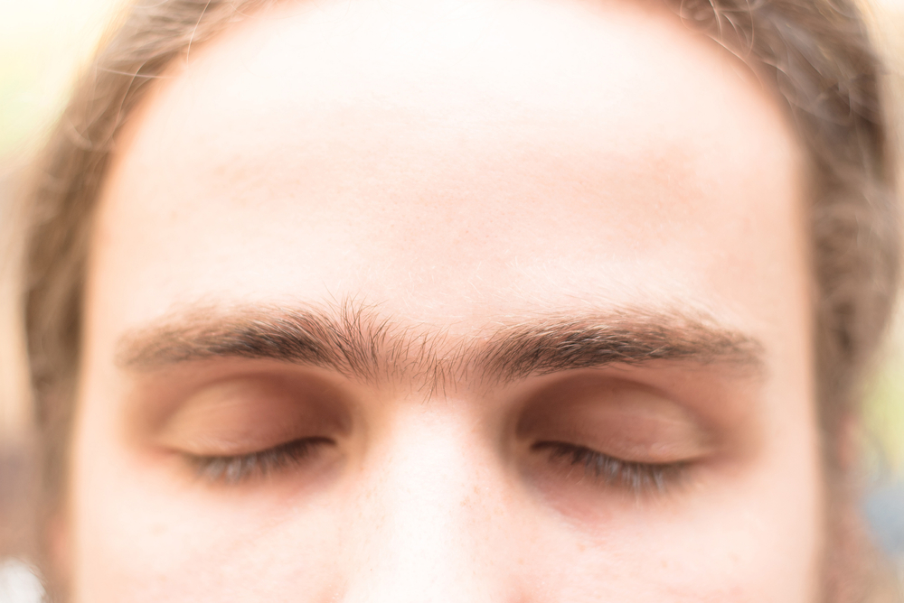 Fused eyebrows of a young man with unibrow of European appearance. The grooming on the face. Men's cosmetology. Soft focus.