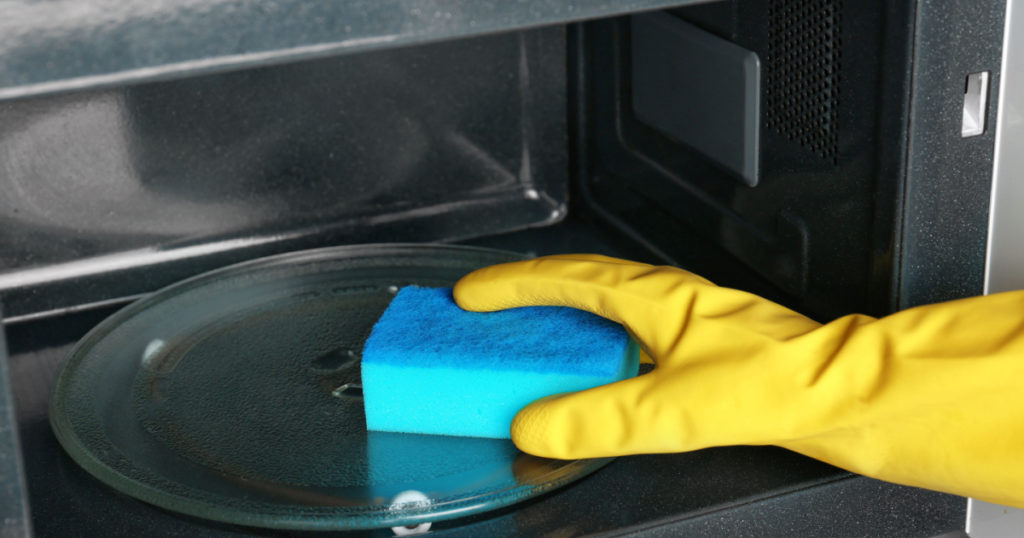 Woman cleaning microwave oven with sponge, closeup