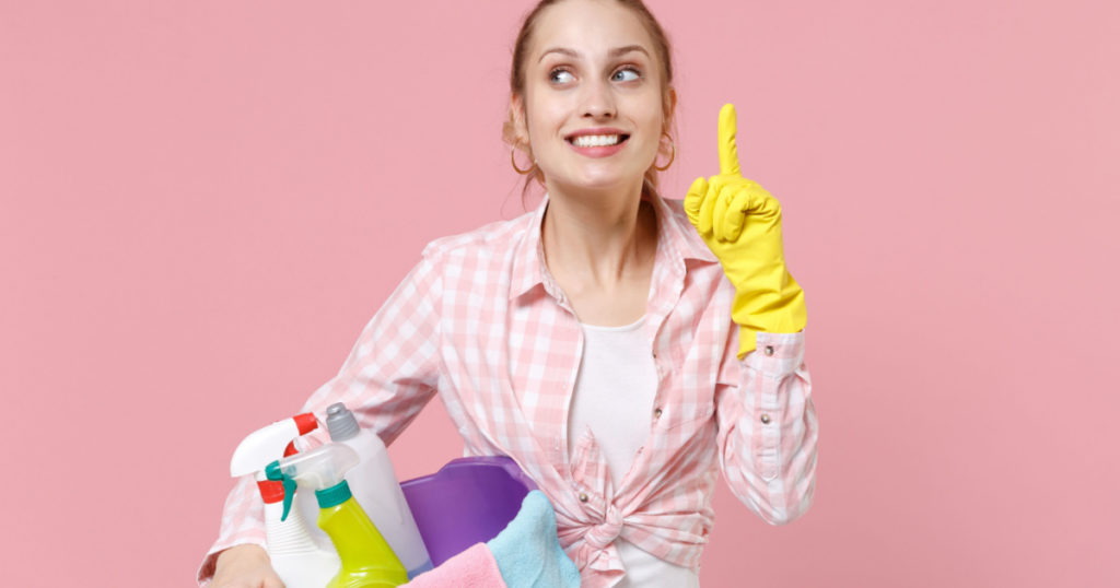 Pensive woman housewife in rubber gloves hold basin with detergent bottles washing cleansers doing housework isolated on pink background. Housekeeping concept. Holding index finger up with great idea