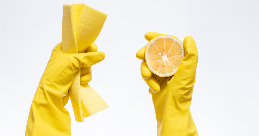 hands in yellow rubber gloves for cleaning hold a rag and lemon on a white background, natural cleaning products for home and kitchen, professional cleaning