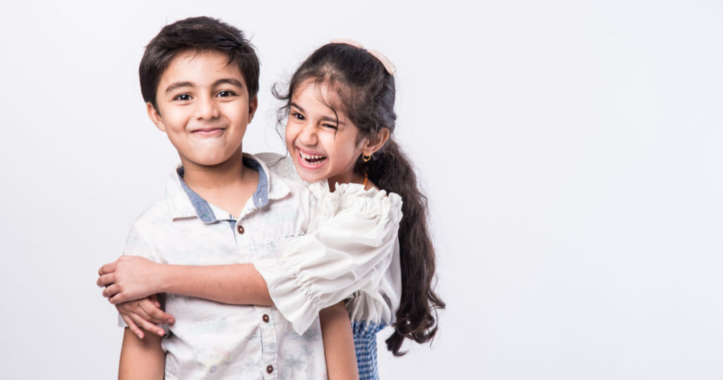 Cute little Indian asian siblings standing and embracing each other in white clothes while standing againstwhite background.