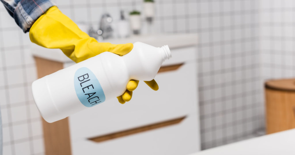 Cropped view of woman holding bottle with bleach lettering in bathroom