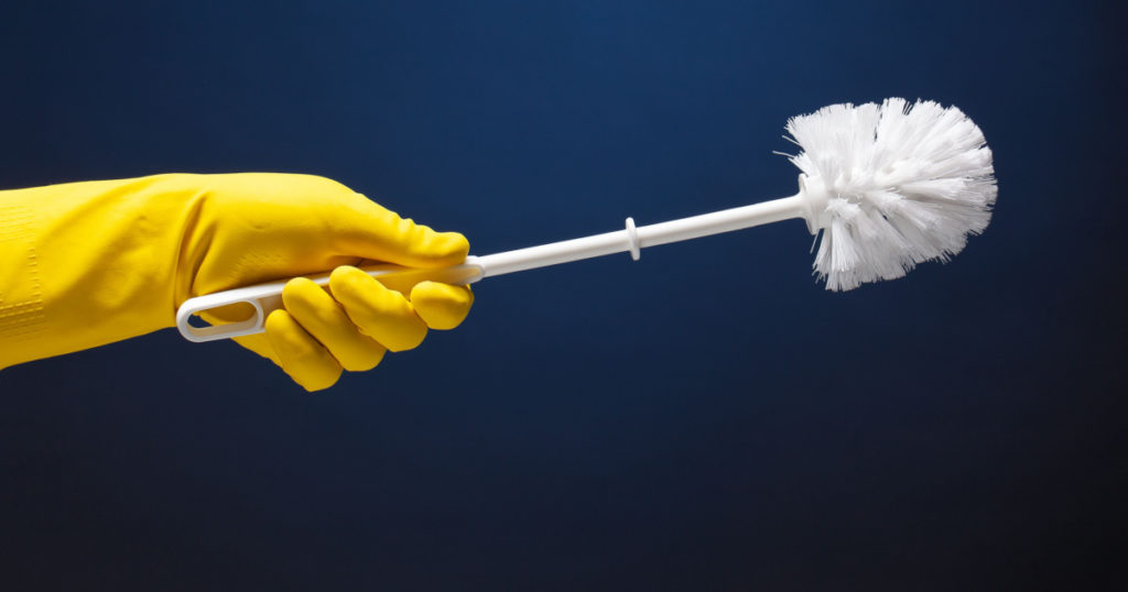 Toilet brush in hand in a yellow rubber glove on a dark background for daily cleaning and hygiene