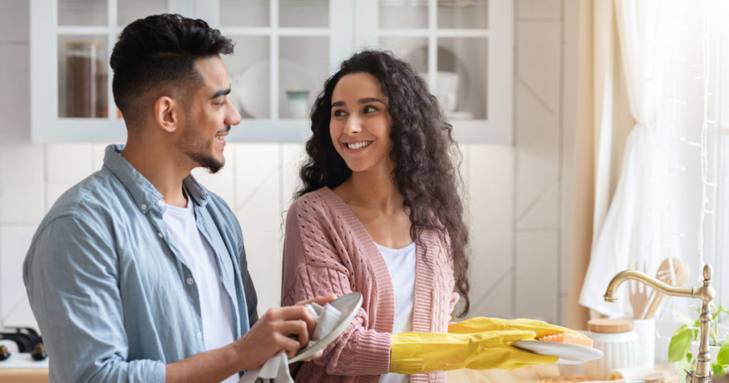 Happy Young Arab Spouses Washing Dishes In Kitchen Together, Loving Middle Eastern Couple Sharing Domestic Chores, Millennial Man And Woman Cleaning Home And Smiling To Each Other, Copy Space