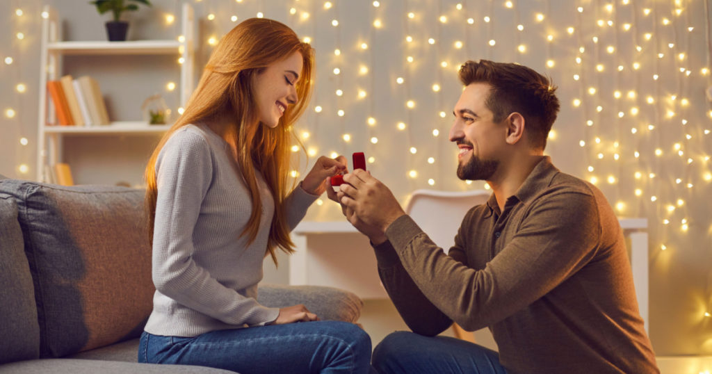 Will you marry me. Couple making love promise to each other on cozy evening at home. Happy woman getting romantic marriage proposal. Young man proposing to girlfriend and giving her engagement ring