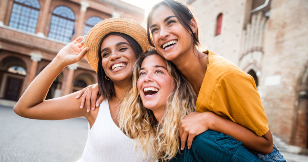 Three young multiracial women having fun on city street outdoors - Mixed race female friends enjoying a holiday day out together - Happy lifestyle, youth and young females concept
