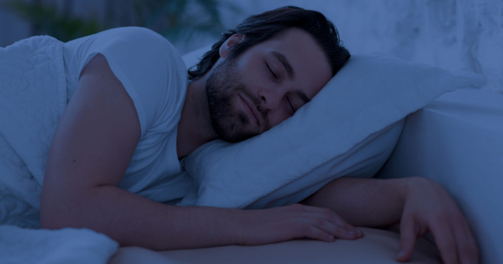 Peaceful handsome bearded young man sleeping in comfortable bed alone at home, enjoying his orthopedic mattress and pillow, side view, copy space. Good sleep concept
