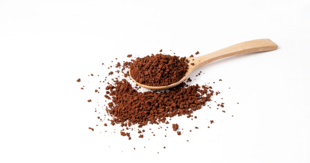 Roasted ground coffee in wooden spoon on white background.